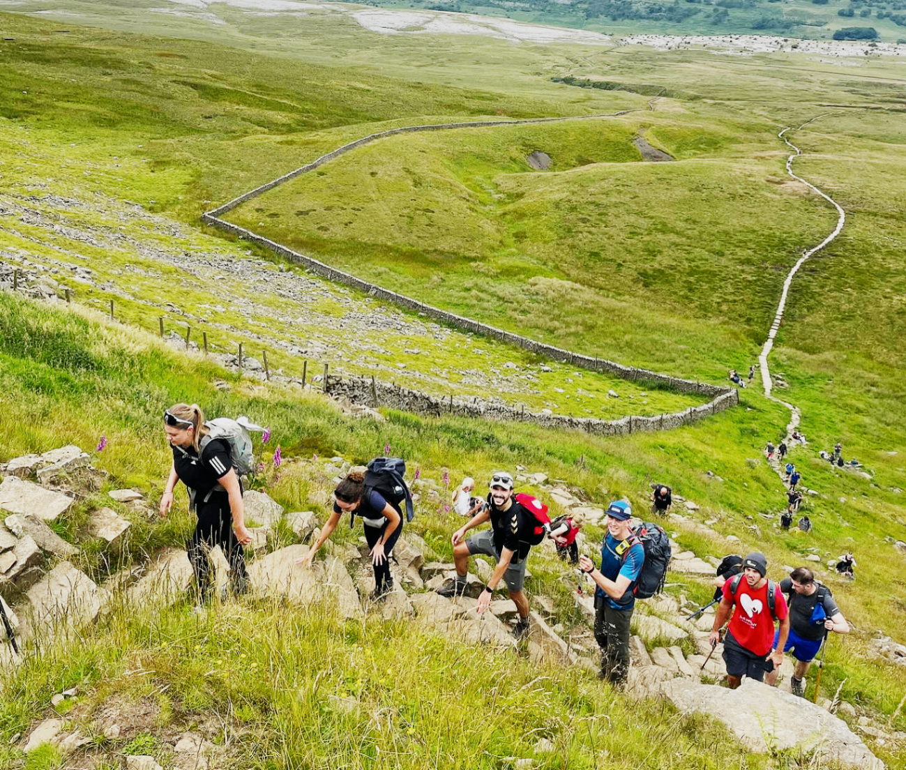 Walkers climbing a rocky section of the Yorkshire Three Peaks route with green hills stretching out below.