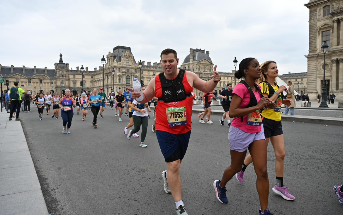 A Mitchy Foundation runner giving a thumbs up as he runs past the Louvre during the Paris Marathon.