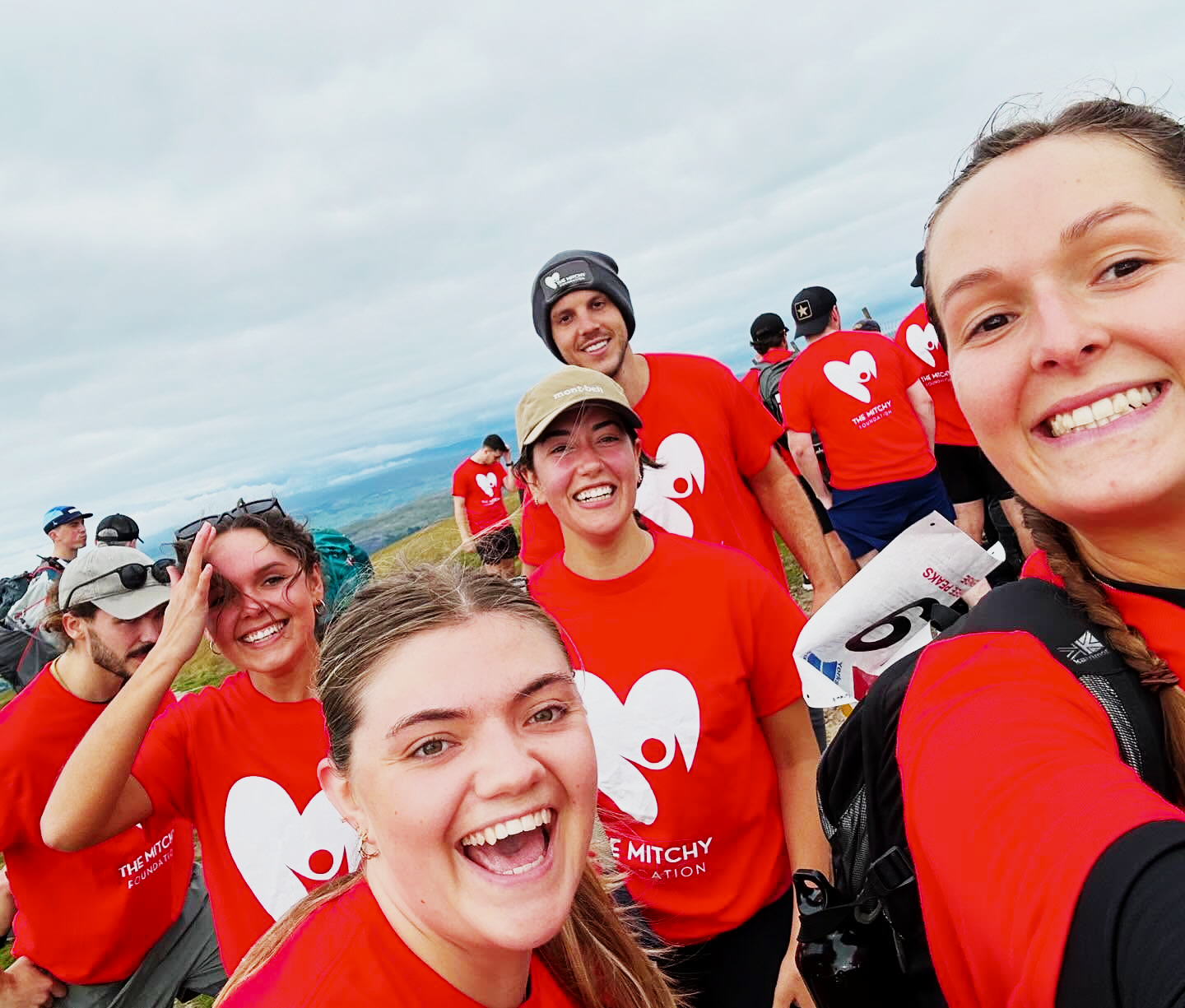 A cheerful summit selfie taken by supporters wearing Mitchy Foundation shirts during the challenge.